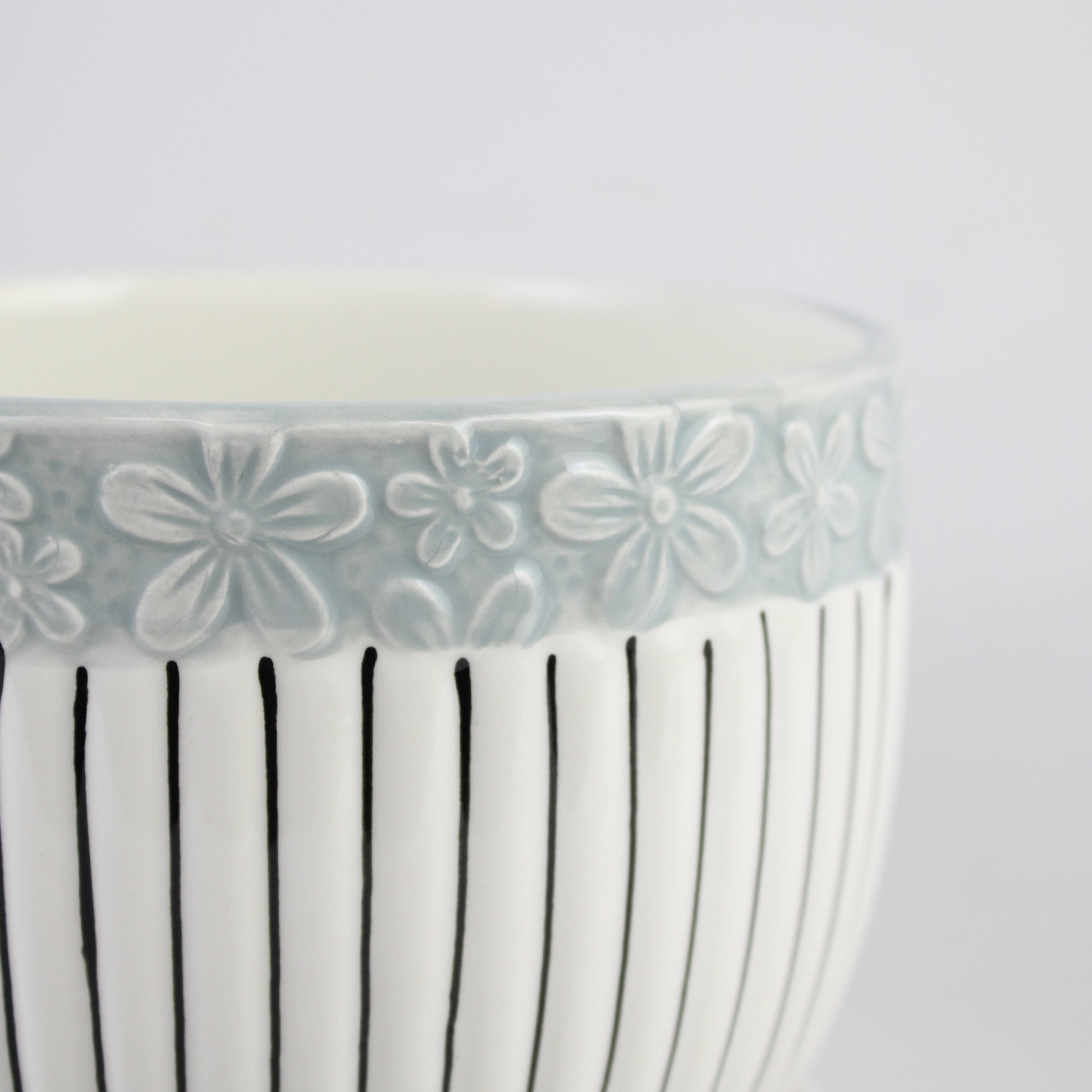 Ceramic bowl with floral pattern on rim and vertical lines on body against a white background