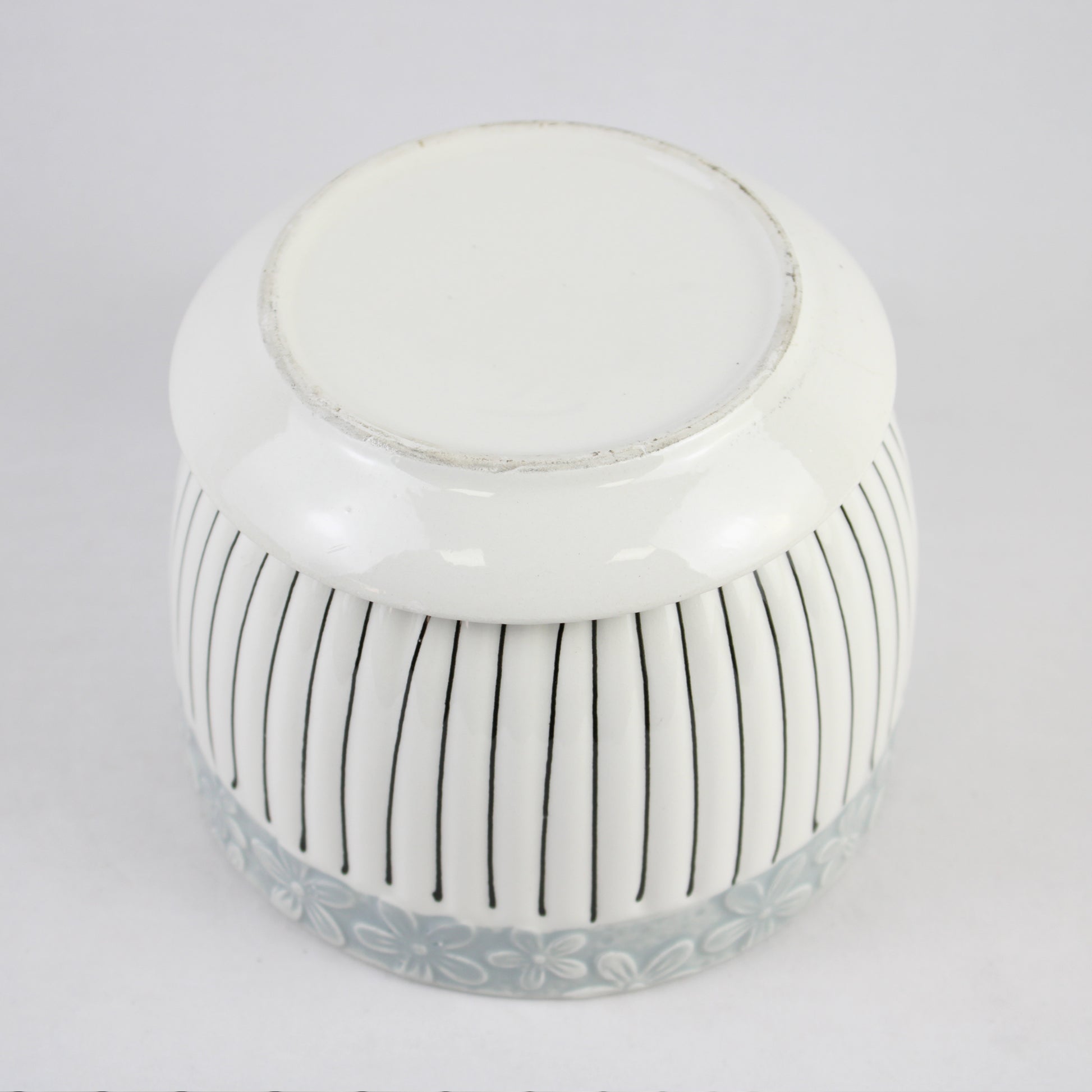 White ceramic jar with black vertical stripes on a light gray background